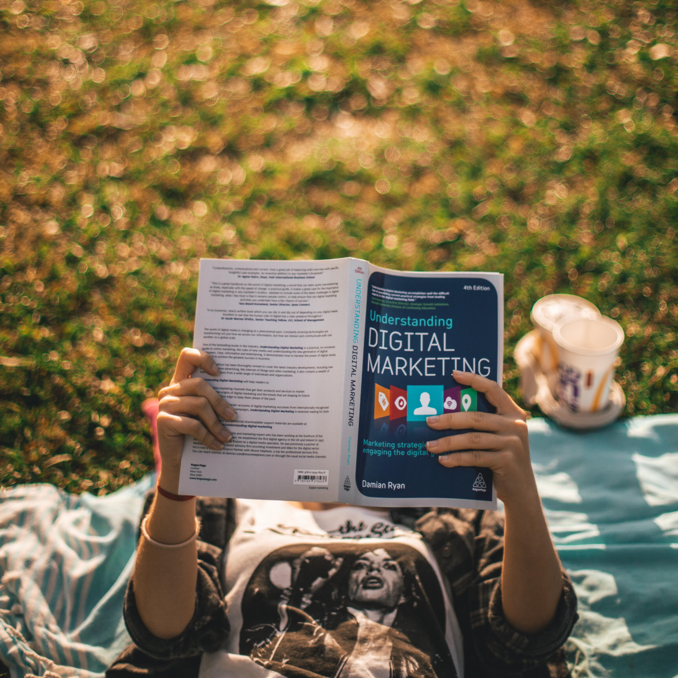 An image with a young lady lying on her back and reading a book about digital marketing.
